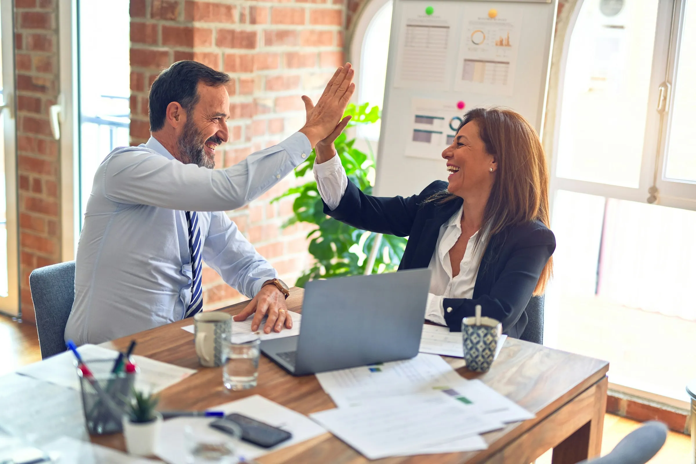 Two recruiters celebrating a closed placement with a high-five at a sunlit desk